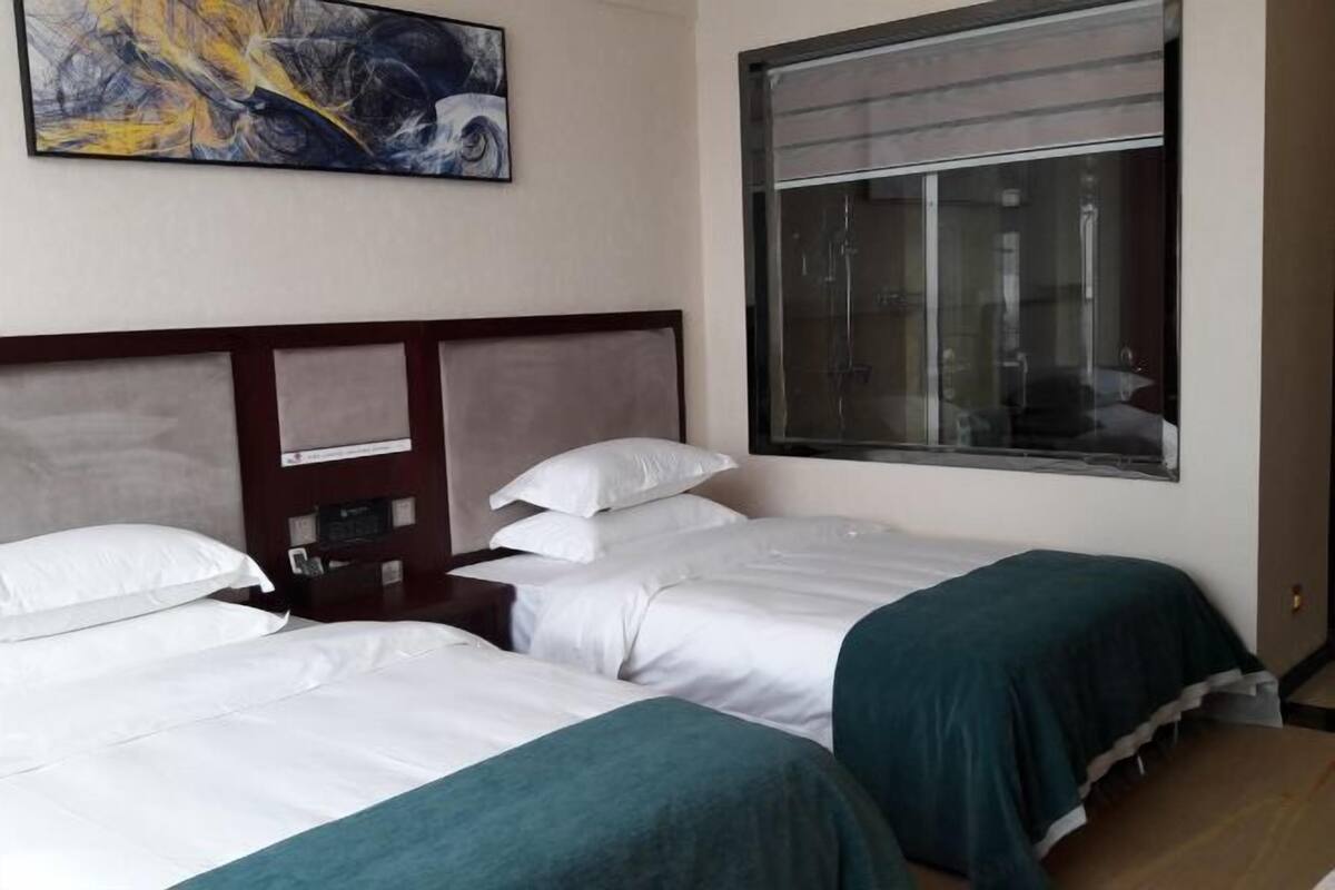 Une chambre d’hôtel avec deux lits simples, une grande fenêtre et un tableau au mur.