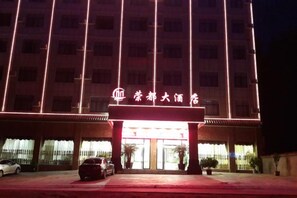 A hotel entrance with a prominent sign, a parking area, and a building facade. - Rongdu Hotel (Yongren)
