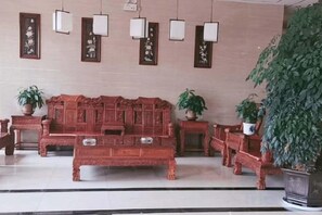 A traditional wooden sofa set with multiple seating options, a potted plant, and wall-mounted light fixtures. - Rongdu Hotel (Yongren)