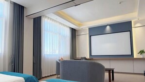 Una camera d'albergo con due letti, un'area salotto, un grande schermo televisivo e una finestra con tende.