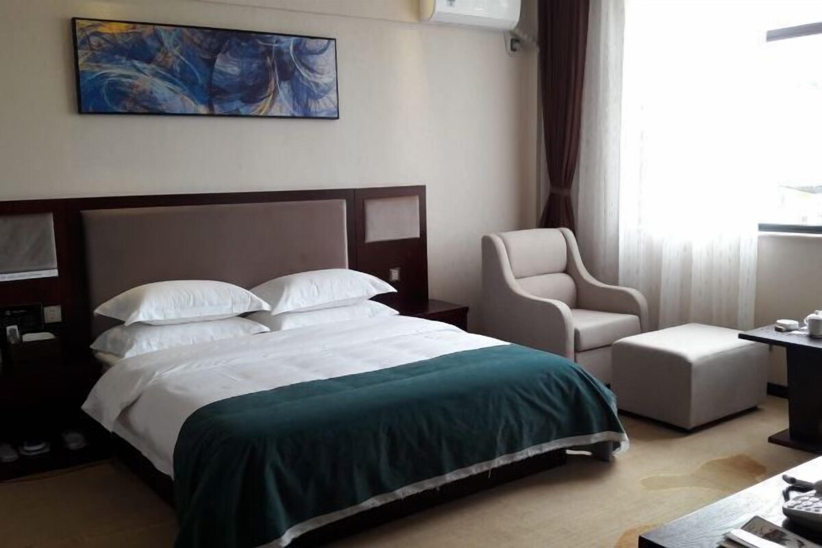 Una habitación de hotel con cama, una silla, un escritorio y un cuadro en la pared.