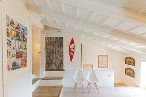 Relax in a cozy space with a high ceiling and exposed beams, featuring a set of chairs and a unique collection of framed items.