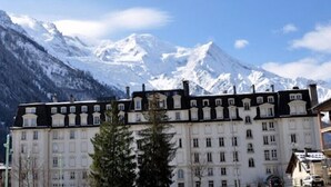 A large, historic building with multiple windows and a symmetrical facade, set against a backdrop of snow-capped mountains. - Nice Apt With Balcony In Chamomix (Chamonix-Mont-Blanc)