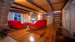 A cozy living room with wooden floors, a brick wall, and a TV. There are two red-covered sofas and a wine rack. - Charming Villa Tomani with pool and jacuzzi (Krmed)