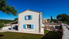 A two-story house with blue shutters, a stone wall, and a paved patio. - Charming Villa Tomani with pool and jacuzzi (Krmed)