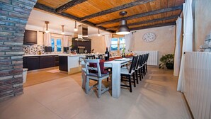 A modern kitchen with a central island, wooden beams on the ceiling, and a dining area with chairs and a table set for a meal. - Charming Villa Tomani with pool and jacuzzi (Krmed)