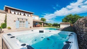 A hot tub with a stone wall and a pool in the background. - Charming Villa Tomani with pool and jacuzzi (Krmed)