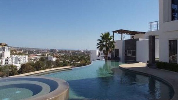 Ett modernt poolområde med en böljande design, en palm och en utsikt över stadssiluetten i bakgrunden.