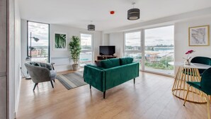 Un salon moderne avec un canapé vert, un fauteuil gris et un coin repas comprenant une table ronde et des chaises.