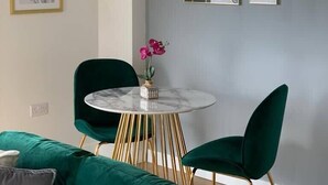Un salon moderne avec une table ronde en marbre, des fauteuils en velours vert et un luminaire suspendu.