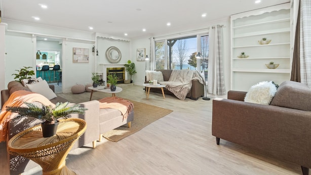 A spacious living room with a sofa, armchairs, and a coffee table. There is a fireplace and a view of the outdoors.