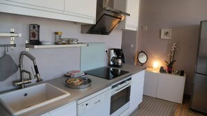 A compact kitchen with white cabinets, a stainless steel range hood, a coffee maker, and a small refrigerator.