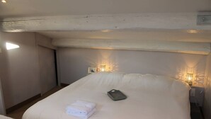 A neatly made bed with a folded towel, a bedside table with a lamp, and a wall-mounted light fixture.