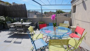 A patio with a round glass table surrounded by colorful chairs, a small potted plant, and a decorative umbrella.
