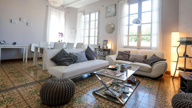 A spacious living room with two white sofas, a glass coffee table, and patterned floor tiles.