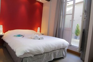 A hotel room with a bed, a nightstand, a lamp, and a view of the outside.