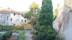 Un étroit sentier menant à un bâtiment à la façade en pierre, avec un arbre grand et mince qui s’y trouve.
