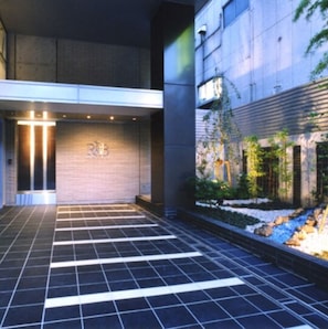 Enter the R&B building through a sleek glass door with a metallic frame, surrounded by a tranquil landscaped area.