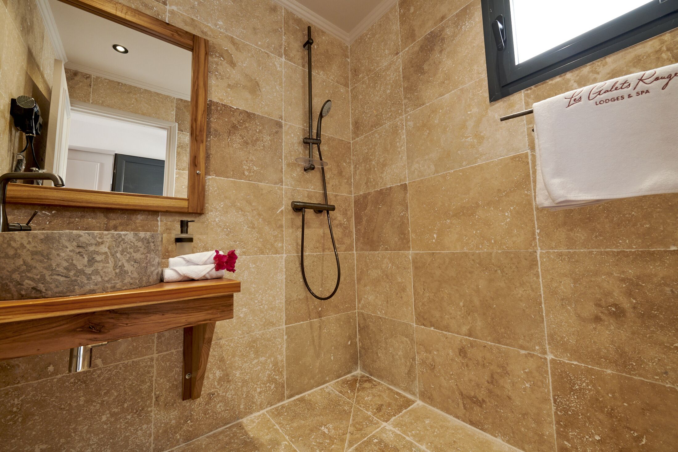 A bathroom with a shower, a wooden vanity, a mirror, and a towel hanging on the wall.