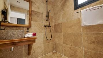 A bathroom with a shower, a wooden vanity, a mirror, and a towel hanging on the wall.