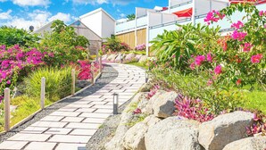 A pathway leading to a modern building with a white facade, surrounded by vibrant pink flowers and greenery. - Les Galets Rouges Lodges & Spa (Bouillante)