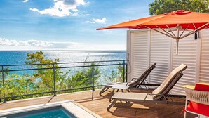 A poolside area with a view of the sea, lounge chairs, and an umbrella. - Les Galets Rouges Lodges & Spa (Bouillante)
