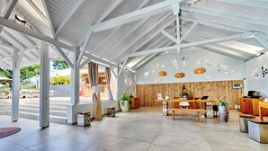 A spacious lobby with a high ceiling, wooden reception desk, and a stone wall. - Les Galets Rouges Lodges & Spa (Bouillante)