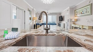 A modern kitchen with a large sink, marble countertops, and a chandelier.