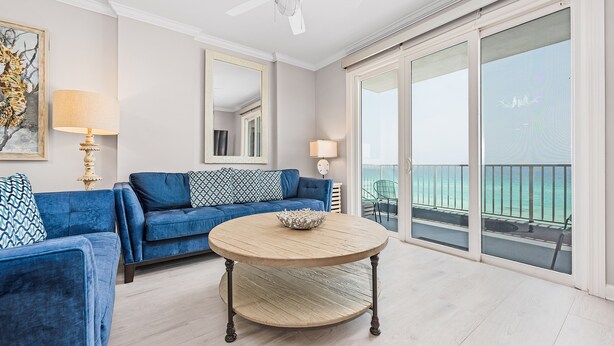 A living room with a blue sofa, a round wooden coffee table, and a large window with a view of the ocean.