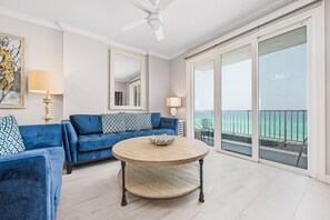 Ein Wohnzimmer mit einem blauen Sofa, einem runden Couchtisch und einem großen Fenster mit Blick auf den Ozean.