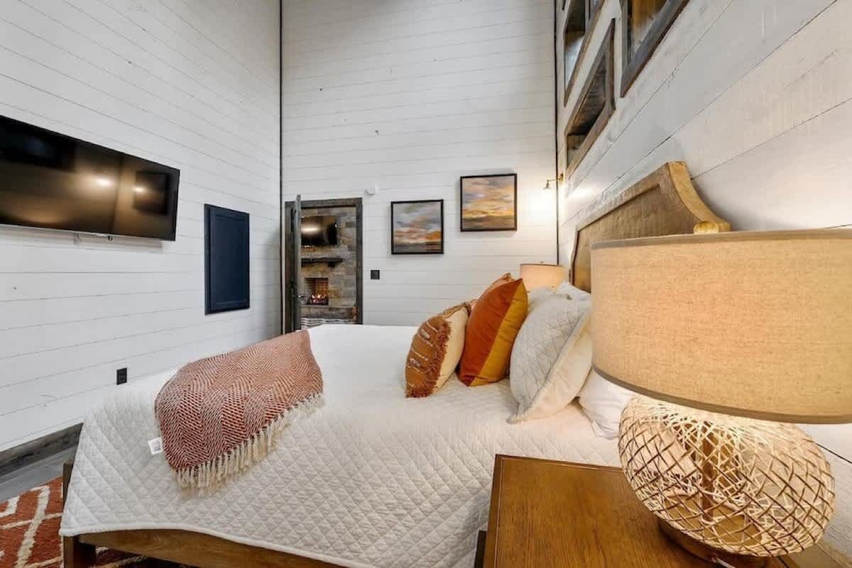 A bedroom with a bed, a TV mounted on the wall, and a fireplace.
