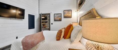 A bedroom with a bed, a TV mounted on the wall, and a fireplace.