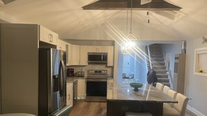 Una cocina moderna con electrodomésticos de acero inoxidable, una isla central con taburetes y una escalera que sube a otro nivel.
