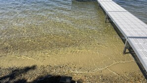 Vista despejada de un muelle que se adentra en un lago con orilla arenosa.