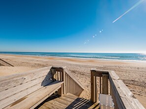 Une promenade en bois qui mène à une plage, avec un ciel dégagé et une mer calme.