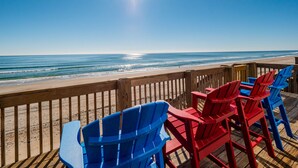 Un pont de fusta amb cadires Adirondack vermelles i blaves que donen a una platja.