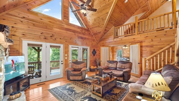 A spacious wooden cabin with a high ceiling, a central seating area with sofas and a coffee table, and a balcony with a view of the outdoors. - Almost Heaven Cabin - River Access! (Murphy)