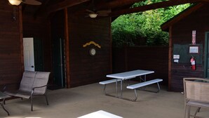 Un espacio al aire libre cubierto con mesas y sillas de picnic, un reloj en la pared y un extintor de incendios montado en la pared.