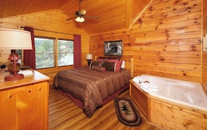 Relax in this cabin-style bedroom with a large bed, wall-mounted TV, and wooden bathtub.