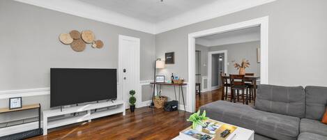 Ein Wohnzimmer mit Flachbildfernseher, grauem Sofa, Couchtisch und Deckenventilator.