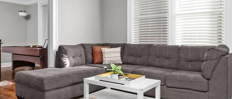 A modern living room with a grey sectional sofa, a white coffee table, and a colorful rug.