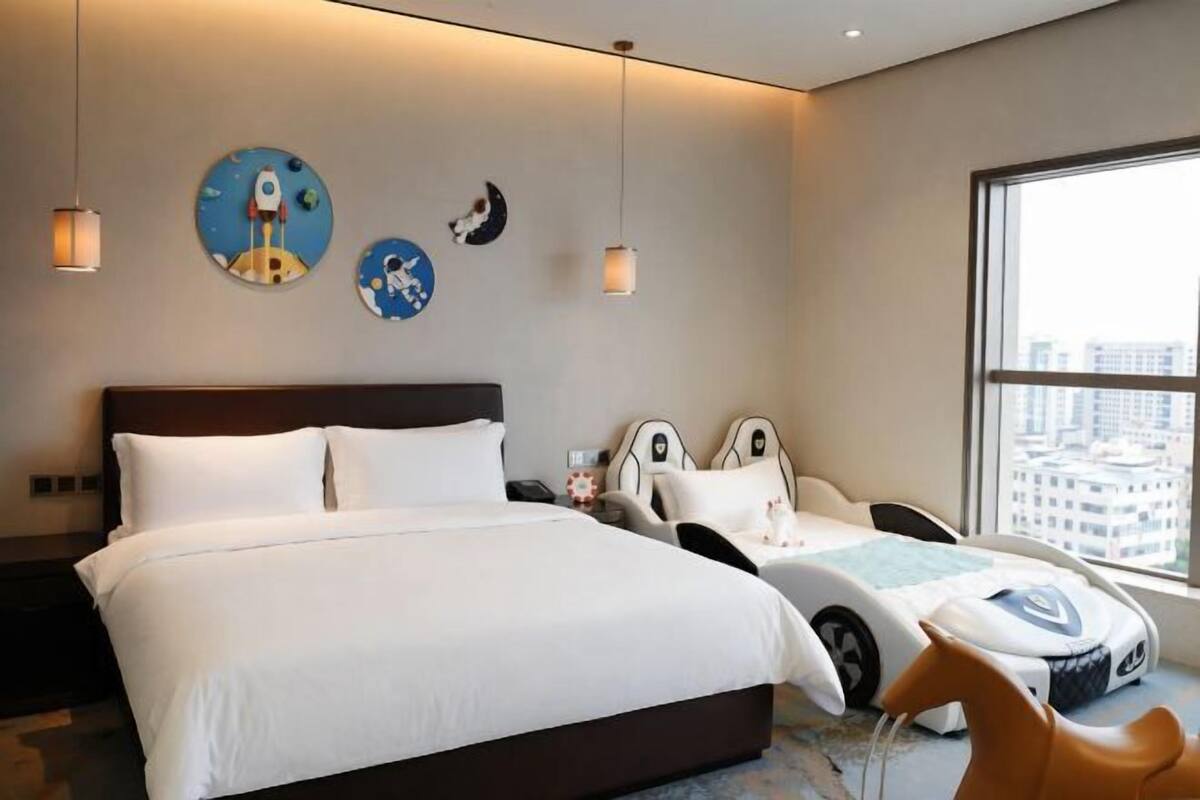 Hotelkamer met een groot bed, twee nachtkastjes, een slaapbank, een raam met uitzicht op de stad en wanddecoratie.