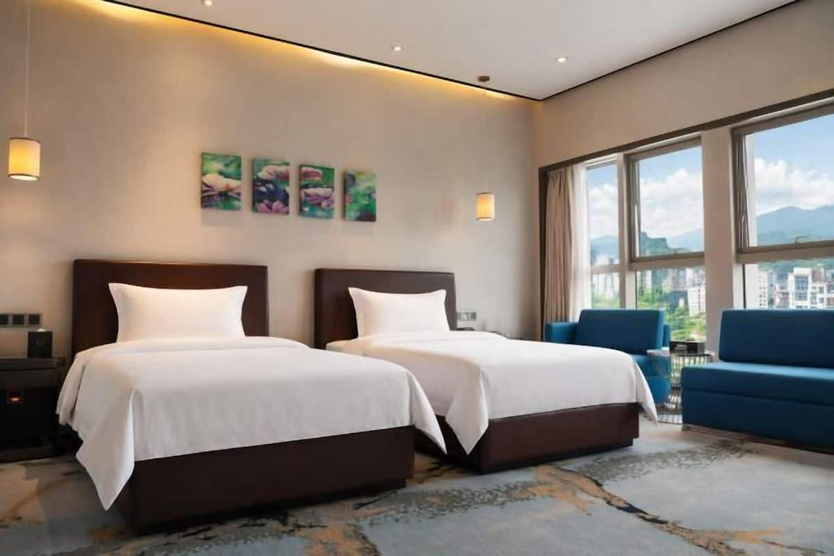 Een hotelkamer met twee bedden, een bank, uitzicht op de stad en kunst aan de muur.