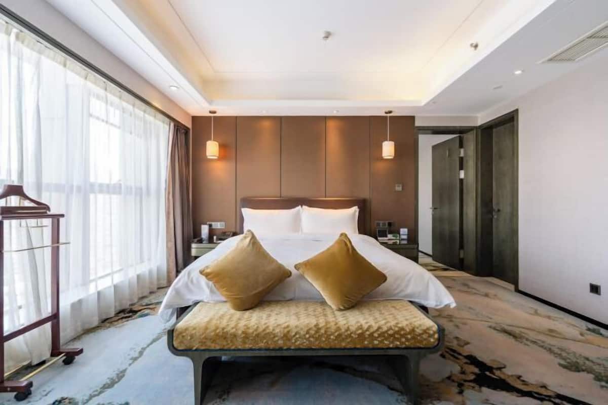 Een hotelkamer met een groot bed, twee kussens, een bankje, een nachtkastje en een kledingkast.