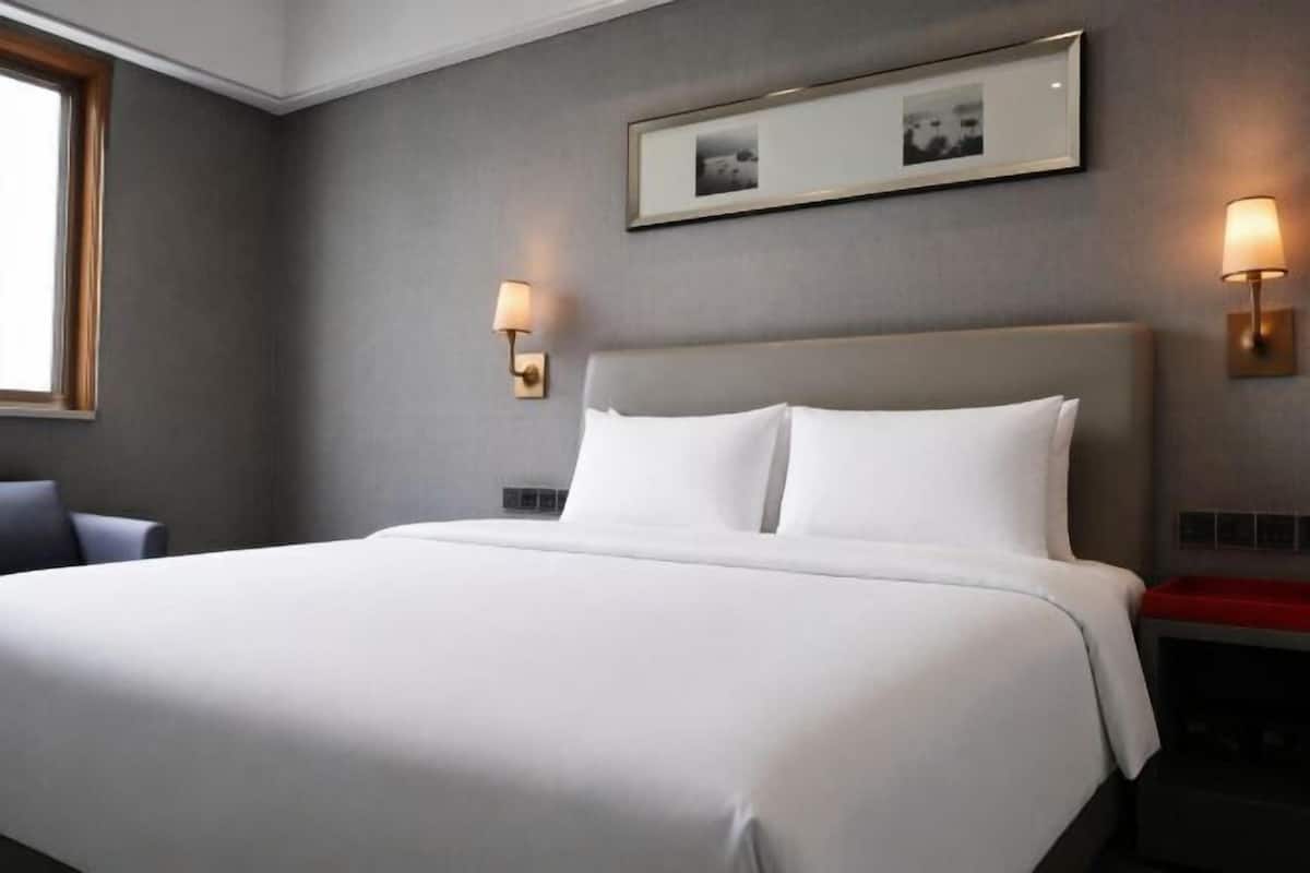 Hotelkamer met groot bed, twee wandlampen, een lijst met foto boven het bed en een raam aan de linkerkant.