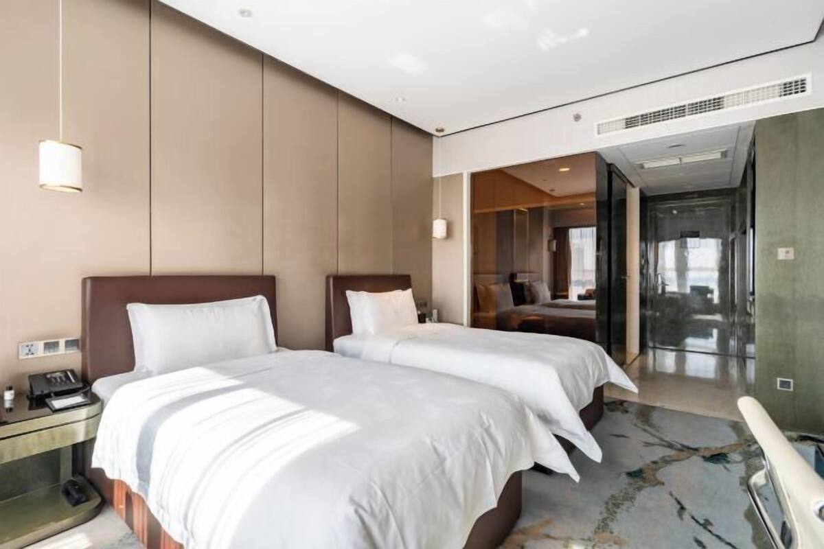 Een hotelkamer met twee bedden, een nachtkastje, een bureau en een badkamer zichtbaar door een glazen deur.