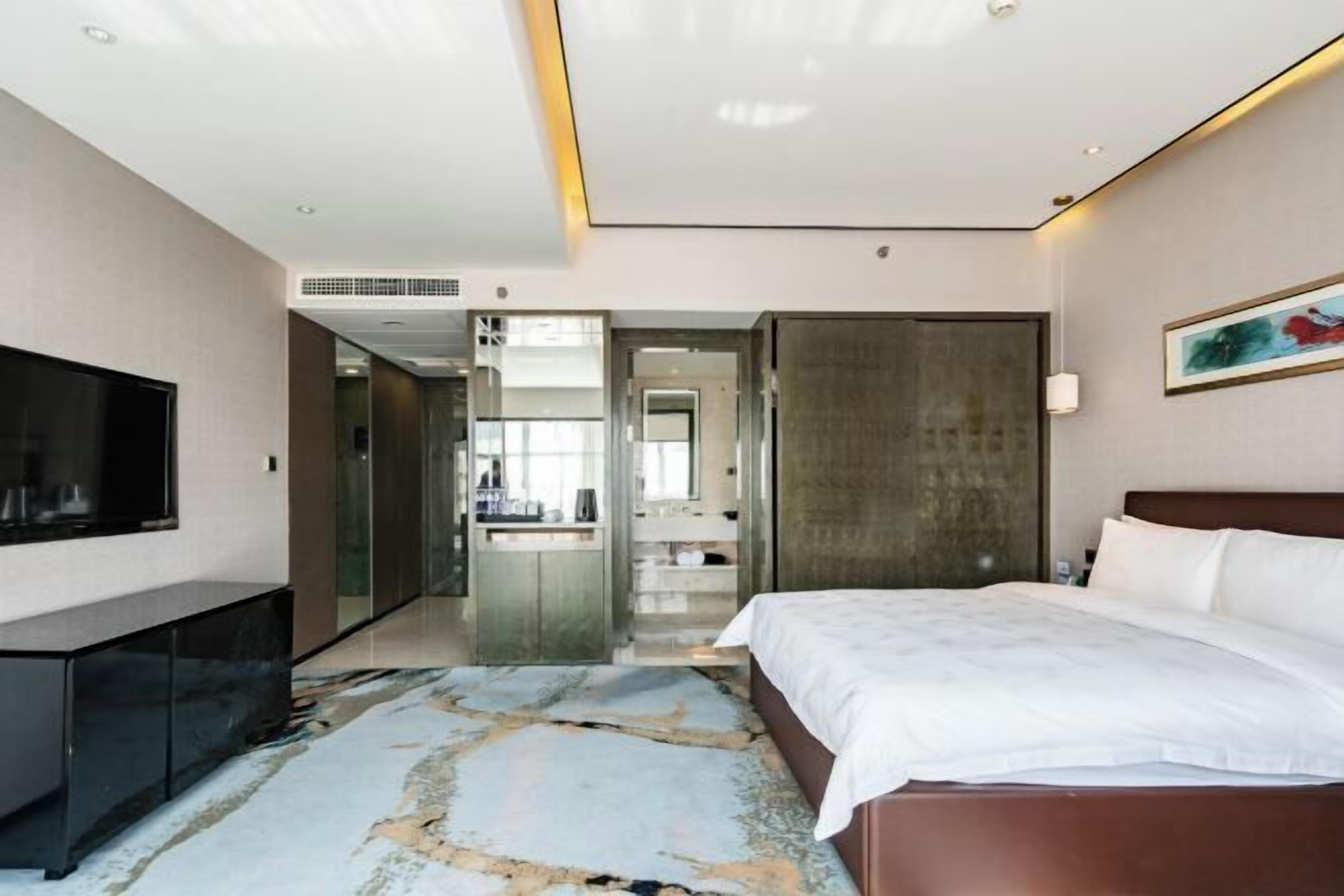 A modern hotel room with a large bed, a flat-screen TV, a desk, and a bathroom visible through an open door.