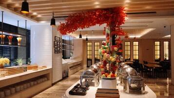 A hotel lobby with a reception desk, a buffet area, and a decorative plant arrangement.