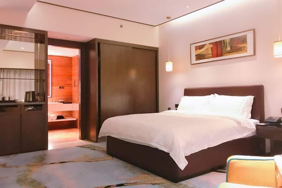 Een hotelkamer met een groot bed, een bureau met stoel, een spiegel en een schilderij aan de muur.