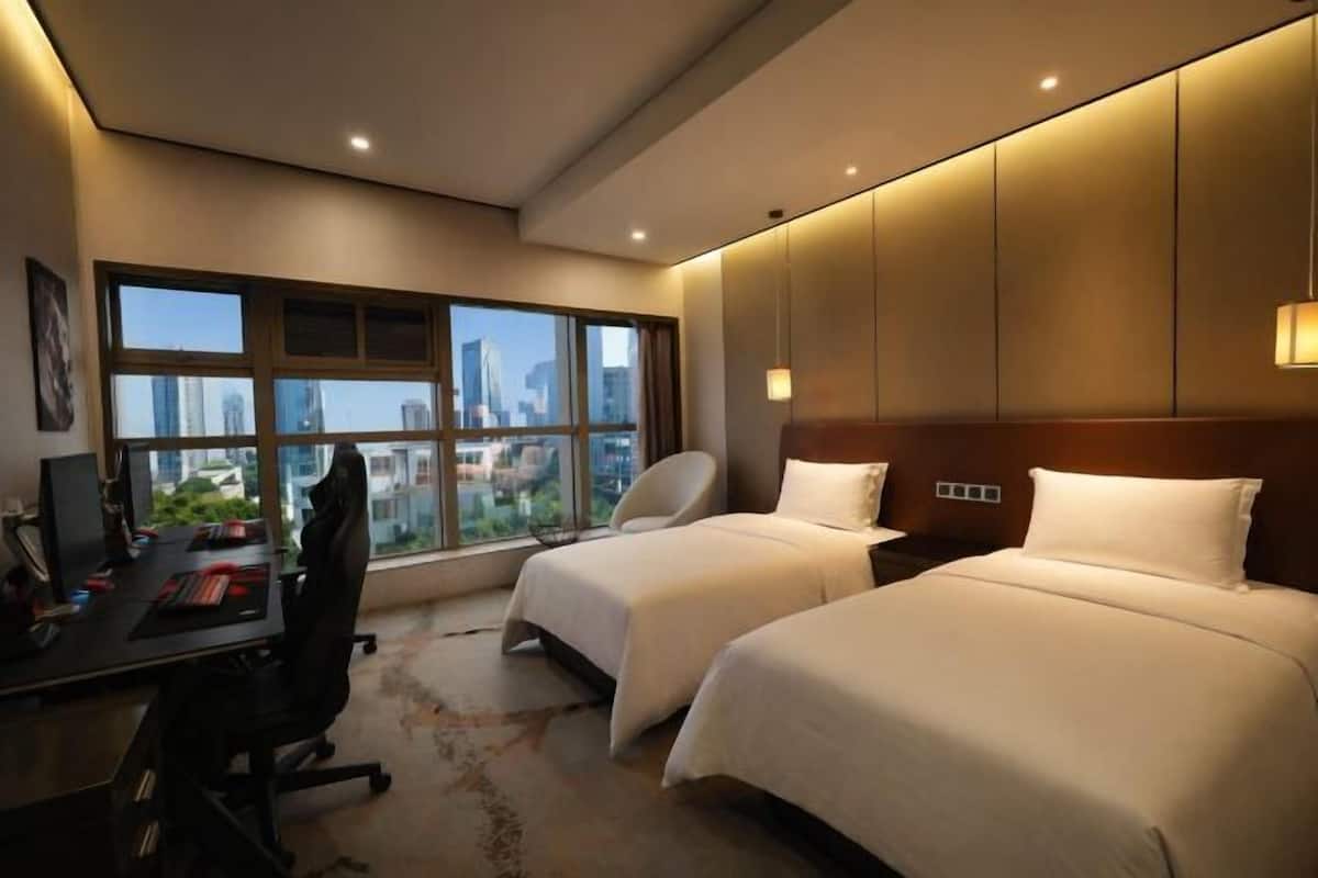Een hotelkamer met twee bedden, een bureau, een stoel en een groot raam met uitzicht over de stad.